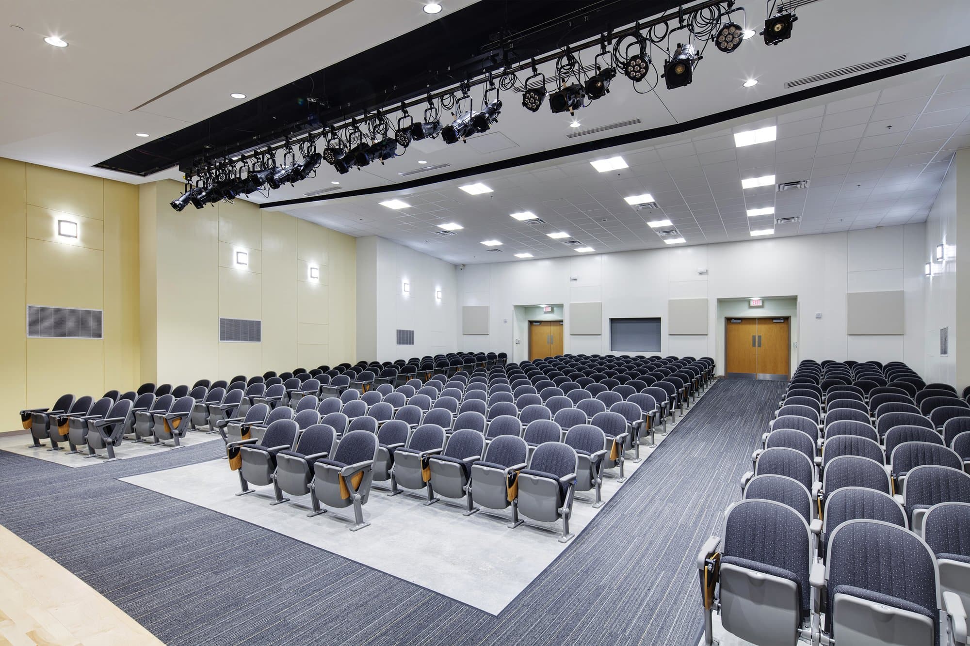Many rows of seats lined up between two aisles of an auditorium leading to exit doors.