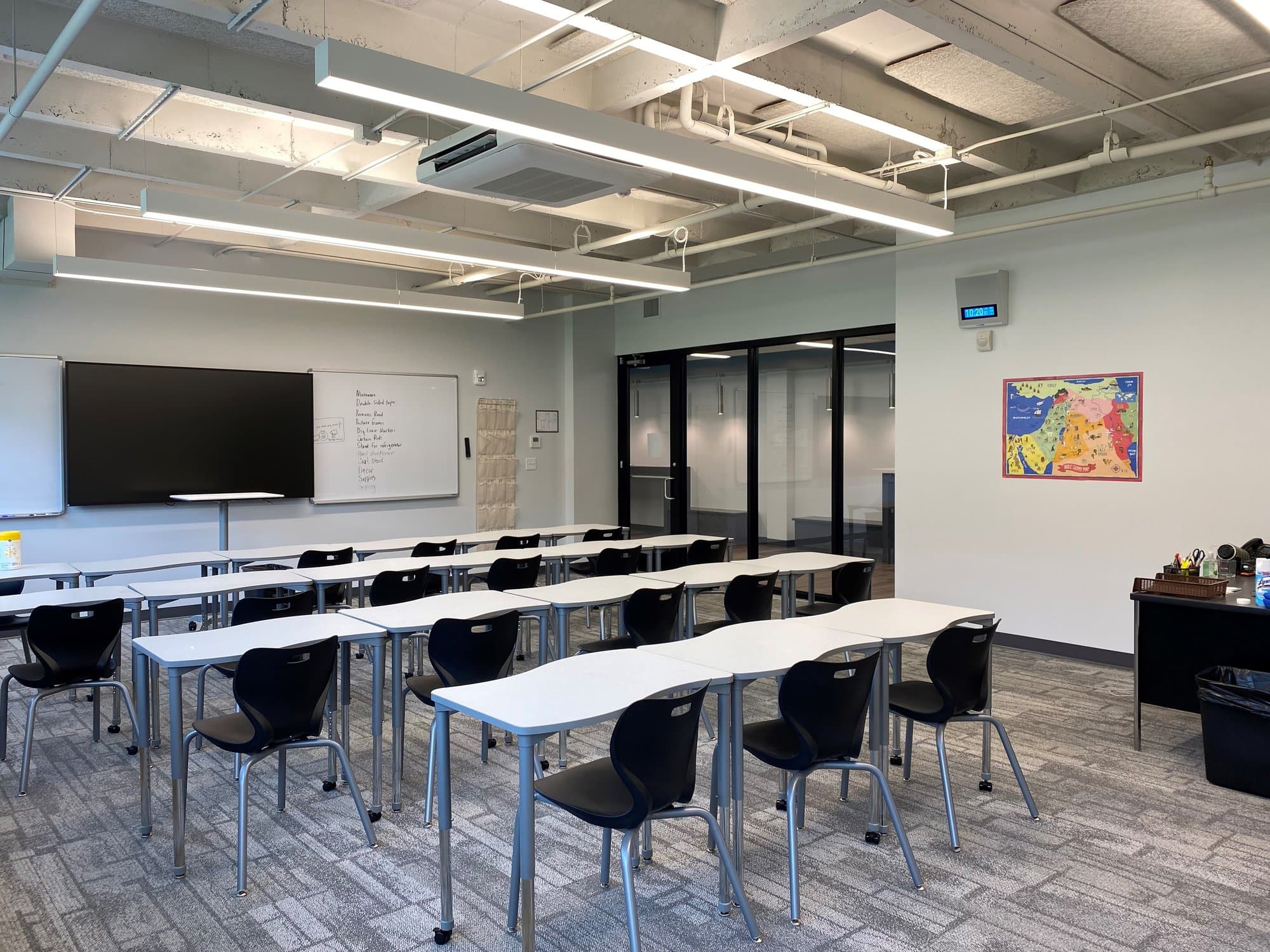White tables lined up in a row contain chairs facing the front of a modern classroom.
