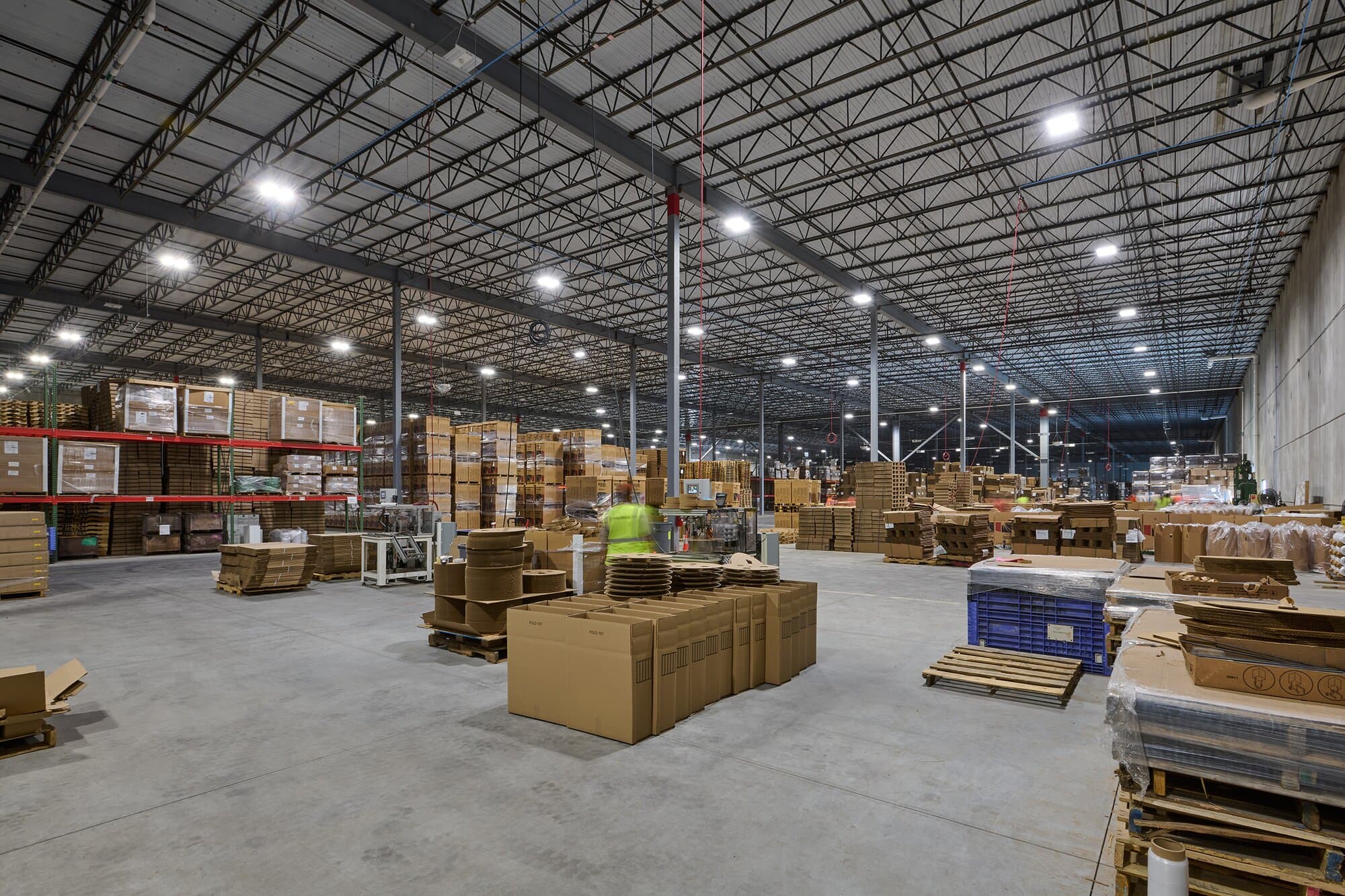 Interior image of warehouse with poured concrete floors, shelving and overhead lighting.