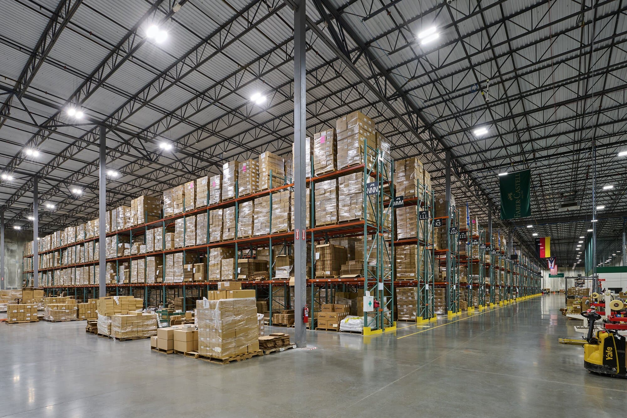 Interior image of warehouse with poured concrete floors, shelving and overhead lighting.